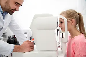 An optometrist is checking a young girl's eyes with an eye machine