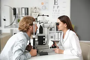 A man and woman wearing white lab coats are looking into a microscope together at an eye clinic