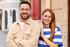 A man and woman smiling and standing with arms crossed in front of a building