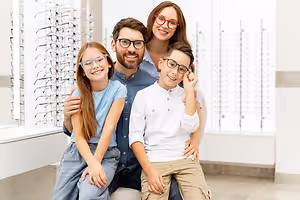A family of four wearing glasses and smiling at the camera in an optical store