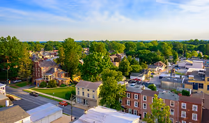 A cityscape view of Lancaster, Pennsylvania, featuring a mix of residential houses, commercial buildings, and lush green trees under a blue sky with scattered clouds, highlighting the vibrant urban landscape.