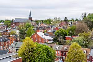 A city view of a neighborhood with trees and houses and a steeple in the distance.