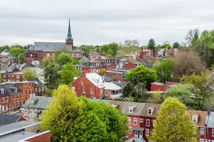 A city view of a neighborhood with trees and houses and a steeple in the distance.