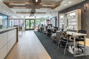 A bright and clean room with chairs, tables, monitors, and lamps, including a reception desk, a glass door, and an exit sign