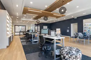 An office space with desks, chairs, monitors, and a lamp.