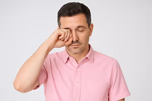Man in a pink shirt rubbing his nose while closing his eyes