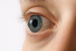 Close-up of a young person's eye with blue iris and visible eyelashes.