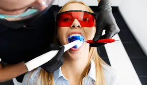 A woman wearing red glasses is having her teeth cleaned by a dentist wearing a face mask and gloves.