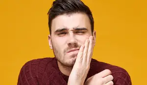 A man wearing a maroon sweater with his eyes closed and his hand on his chin