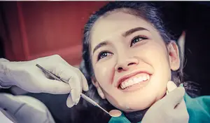 A young girl is smiling and looking at a dentist who is examining her teeth with a dental tool.