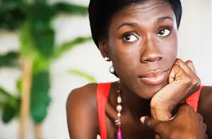A woman wearing a red sleeveless top and a necklace with a hand on her chin