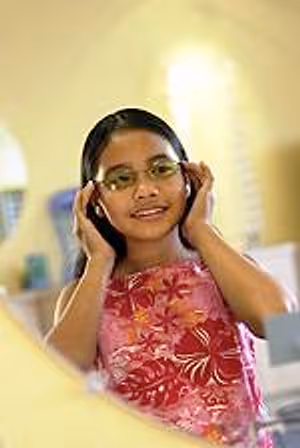 A girl with glasses is smiling and posing for a photo in front of a mirror.