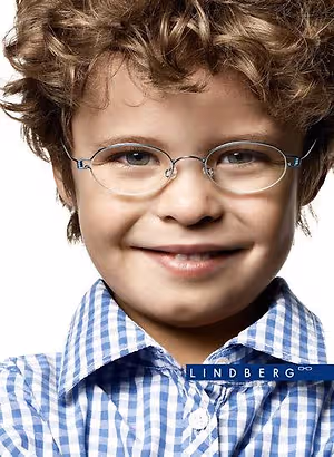 A young boy with curly hair wearing glasses and a blue and white checkered shirt with the word Lindberg on it.