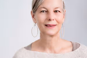 Close-up of a woman with gray hair, wearing earrings, smiling, and looking at the camera