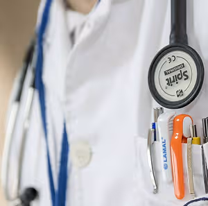 A doctor wearing a white coat with a stethoscope and various tools in their pocket.