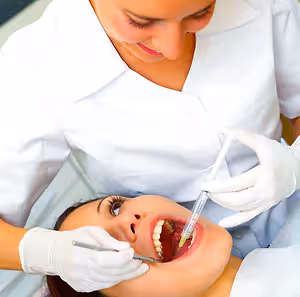 A dentist in white gloves and a mask is performing a dental procedure on a patient in a dental clinic.