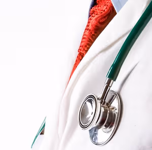 A doctor's white coat with a red tie and a stethoscope in a close-up view