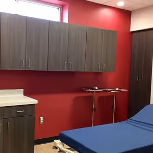 A hospital room with red walls, a bed, cabinets, a window, and medical equipment.