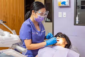 A dental hygienist wearing PPE is cleaning a patient's teeth.