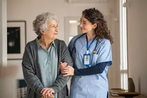 An elderly woman holding a cane standing with a nurse in a nursing home