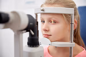 A young girl wearing a phoropter is examining her eyes at an optometrist's office