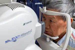 An older man is using an eye examination machine to check his eyes