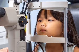a young girl having her eye examined by an optometrist using a slit lamp
