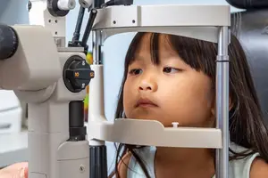 a young girl having her eye examined by an optometrist using a slit lamp