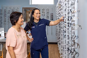 Two women in a store with eyeglasses on display on the wall