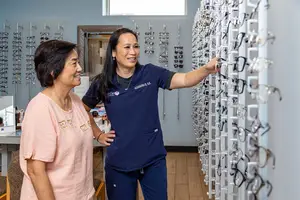 Two women in a store with eyeglasses on display on the wall