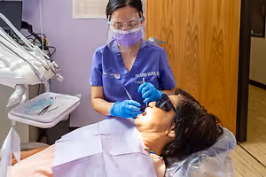 An Asian female dentist wearing a mask, goggles, and gloves, performing dental treatment on a female patient in a dental clinic.