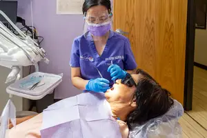 An Asian female dentist wearing a mask, goggles, and gloves, performing dental treatment on a female patient in a dental clinic.