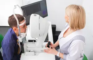 An eye doctor is examining a patient's eyes using an eye examination machine in a clinic.