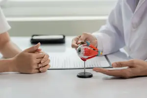 A doctor and a patient are sitting on a desk with an eyeball model on it.
