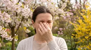 Woman rubbing her irritated eyes outdoors amid blooming flowers