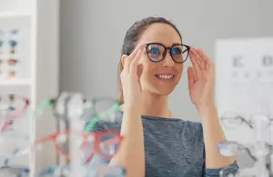 A woman in a gray shirt trying on glasses in a store