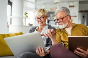 A man and woman sitting on a couch and using a laptop and tablet