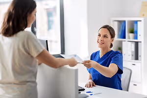 Two women are exchanging papers at a desk in a medical office.