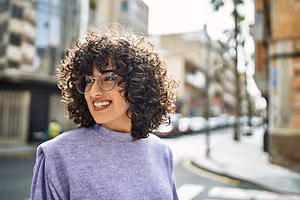 Woman with curly hair, wearing glasses, smiling and standing in a street