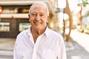 A smiling elderly man in a white shirt standing outside on a city street with blurry background