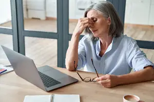 A woman sitting at a desk and looking tired and rubbing her forehead with her hand
