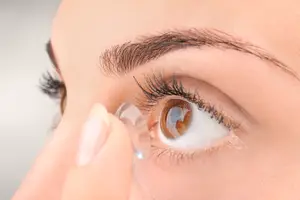 A woman is holding a contact lens and placing it on her eye.