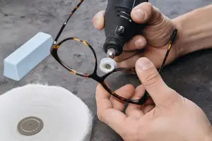 A person is using a black-colored machine to polish the glasses frame in their hand.