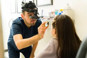 A male optometrist is checking a female patient's eye with a magnifying glass.