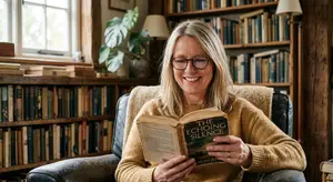 A smiling woman sits in a leather chair reading a book in a cozy room with a bookshelf in the background