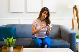 A woman is sitting on a couch and using a contact lens solution.