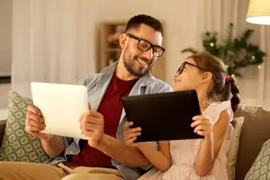 Man and girl sitting on couch looking at a tablet