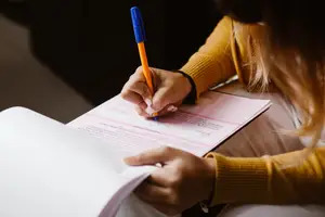 A woman sitting on a chair and writing on a paper with a pen