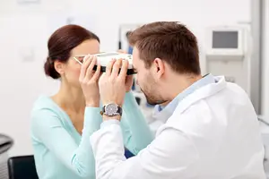 A man with a white coat is examining a woman's eyes with a device