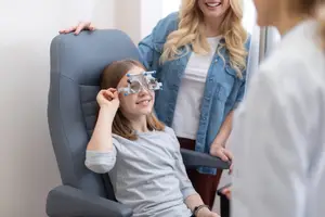 A young girl with glasses and a woman behind her is looking at something in front of her while smiling
